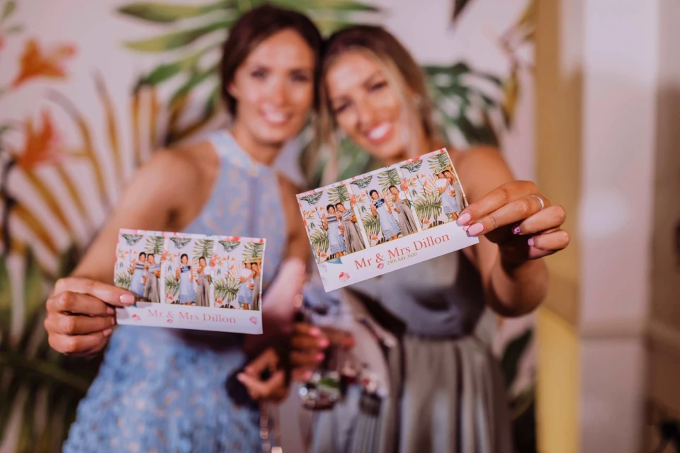 Twee jonge vrouwen showen hun gemaakte photobooth-strips tijdens een feest in de tuin.