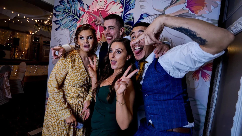Vriendengroep viert feest in glamoureuze outfits met photobooth foto's in de hand.