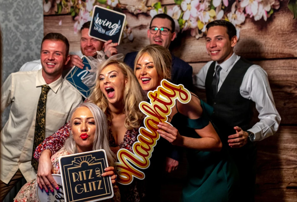 Groep vrienden met props voor een  muur lacht met hun gemaakte photobooth-strook.