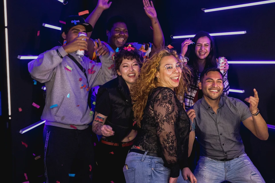 Groep vrienden op dansvloer met neonlichten geniet van een avondfeest met photobooth.