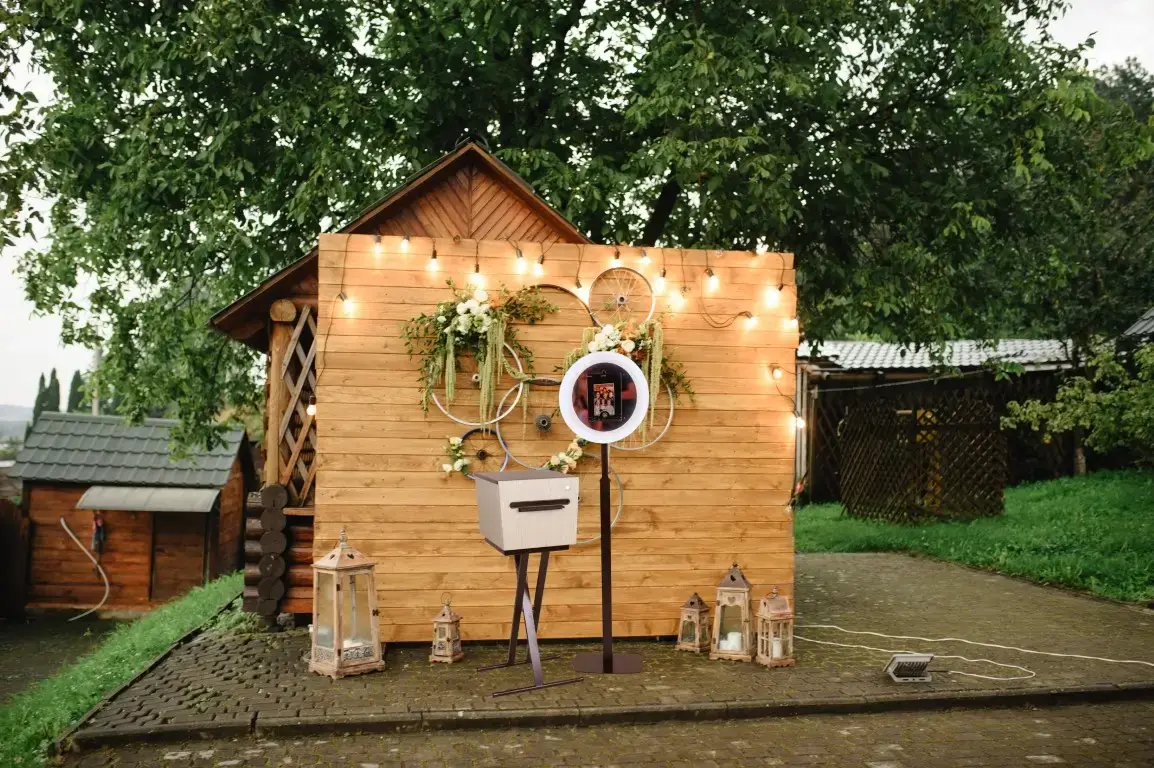 Buitenopstelling met photobooth voor een rustieke houten muur met planten en een feestelijke sfeer.