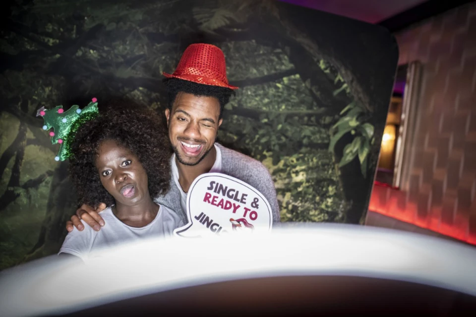 Kerstviering met twee gasten voor een sneeuwdecor, vrolijk poserend met photobooth-foto&rsquo;s.