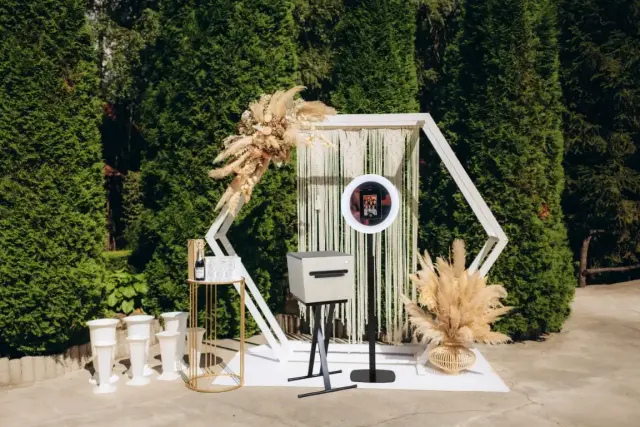 Moderne buitenachtergrond van houten latten met bloemen en een photobooth centraal geplaatst.
